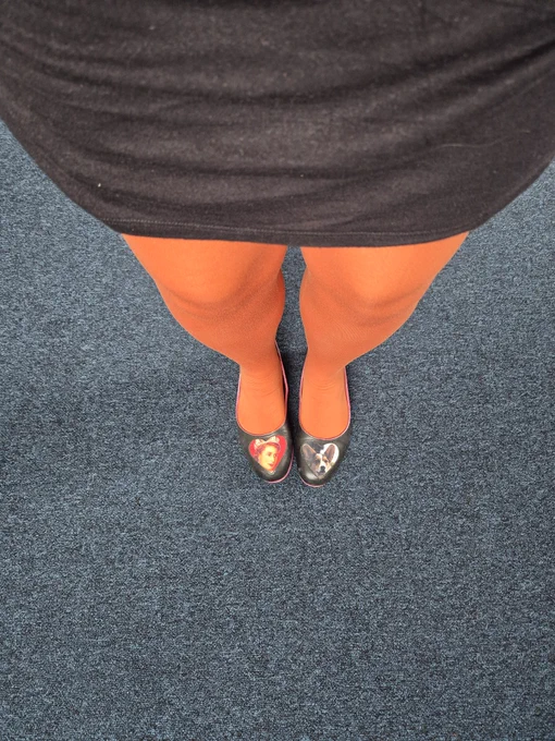 Leg selfie showing black dress, mid-tone orange tights and black ballet pumps. The Irregular Choice ballet pumps have a photo of Queen Elizabeth II on the left foot and a photo of a corgi on the right foot.