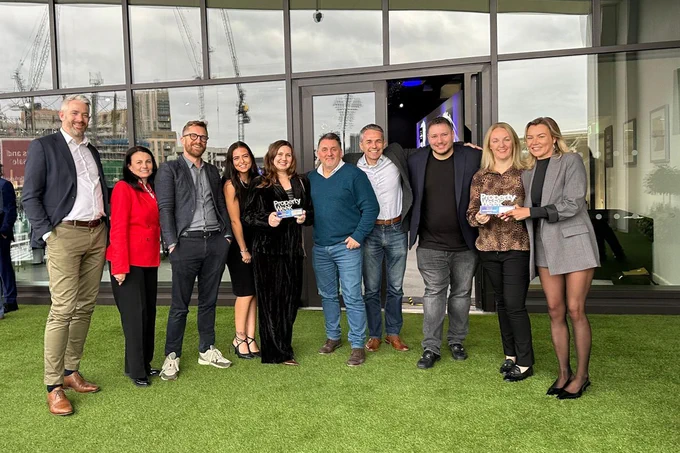 Group of people holding awards standing outside a building, smiling for a photo. Some individuals are dressed in business casual attire.