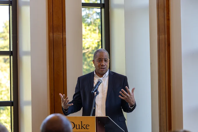 Mo Green stands behind a lectern with a microphone and speaks to an audience. 