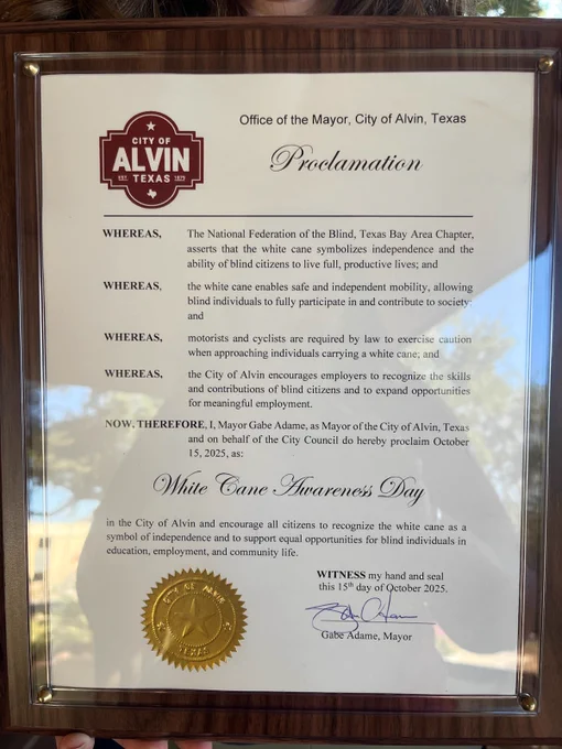 A framed proclamation from the City of Alvin, Texas, designating October 15, 2025, as White Cane Awareness Day. The document is from the Office of the Mayor and includes several “WHEREAS” statements recognizing that the white cane symbolizes independence and enables safe, independent mobility for blind individuals. It encourages motorists, cyclists, and employers to respect and support blind citizens. The proclamation is signed by Mayor Gabe Adame and bears the official city seal in gold at the bottom.
