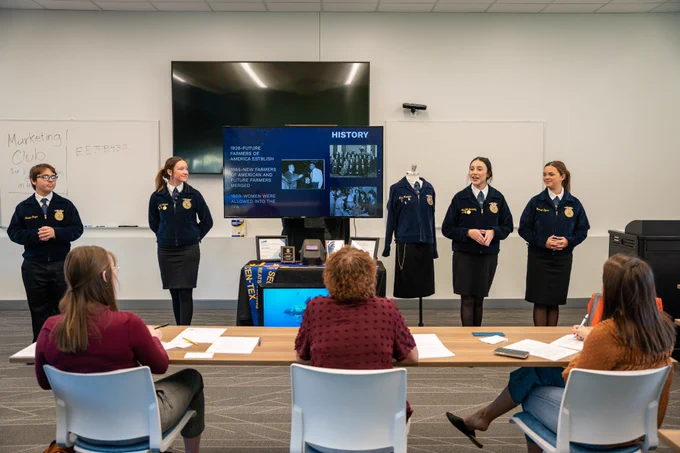Four FFA students in blue jackets give a presentation to a group of judges.
