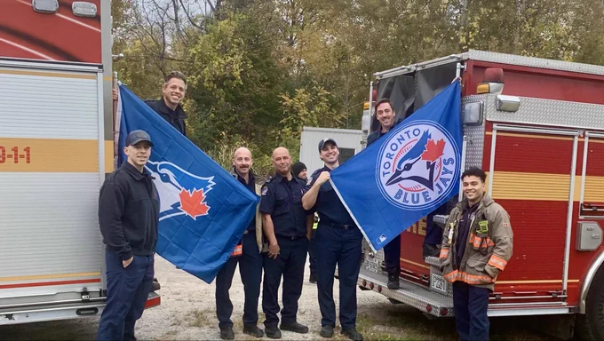 Toronto Fire Services crew members standing in front of two Toronto Fire Services fire trucks holding Toronto Blue Jays flags.