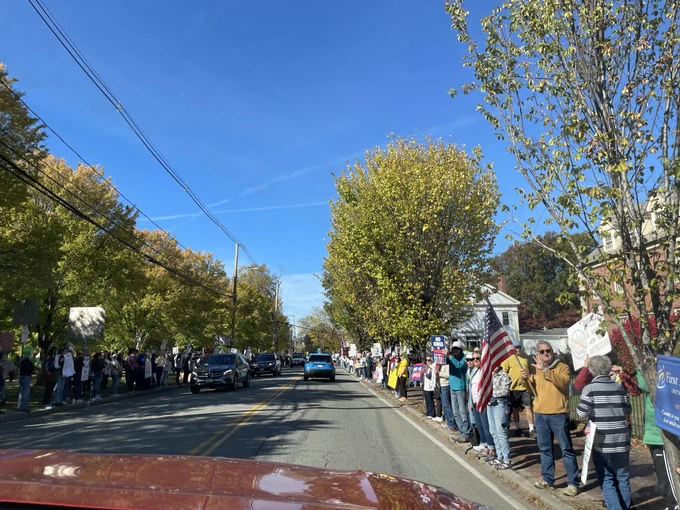 Protesters carrying American flags line both sides of a long road.