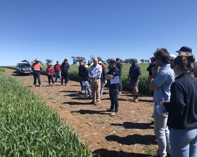 Group of people attending an agricultural field demonstration under a clear blue sky.