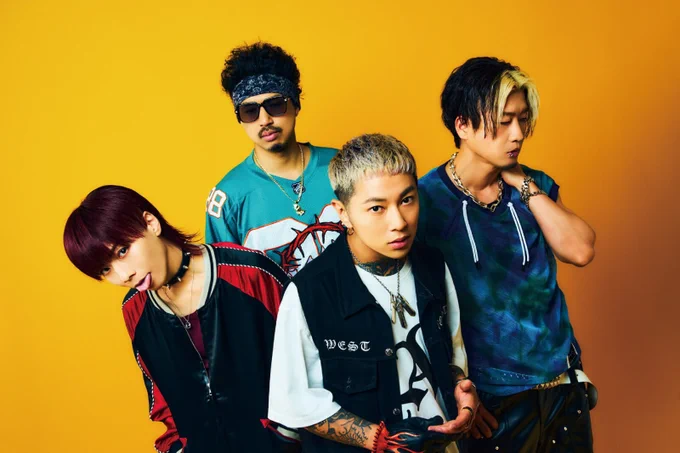 Band photo of ASH DA HERO featuring four members standing together against a vibrant yellow/orange background. They each wear different shirts in different colours, which reflect their characters.