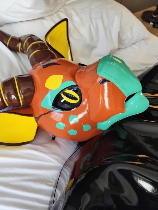 A cute rubber clad toy on a bad with a orange, yellow and green inflatable dragon hood on