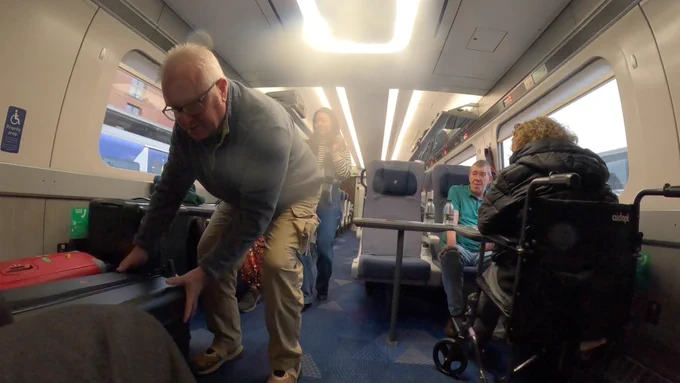 A gentleman manhandling suitcases in the wheelchair space. 