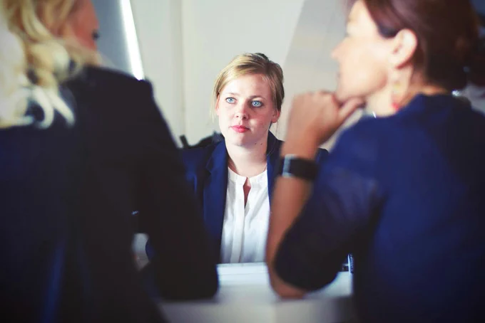 A professional meeting in progress, with three individuals engaged in a conversation around a table. Photo by Unsplash.