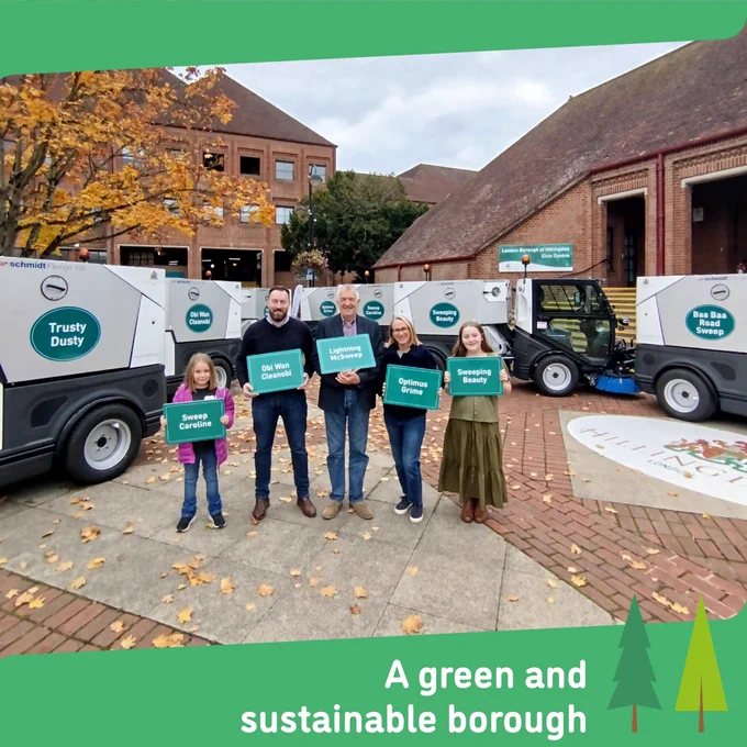 Photo shows the competition winners, two young girls, a man and a woman stood with Cllr Lavery in front of seven street sweeping machines. They are holding boards with the winning names they suggested for each sweeper.