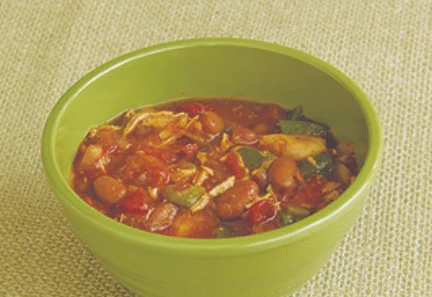A bowl of vegetable and bean soup on a textured beige tablecloth.