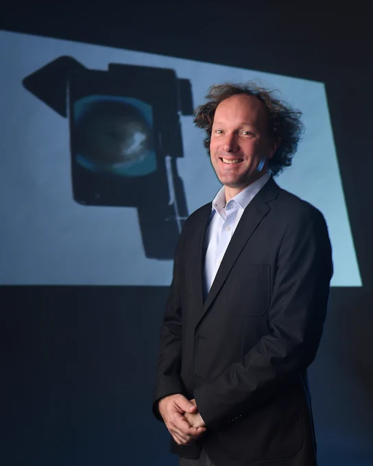 A portrait of Fletcher in 2017 in front of a projection screen of a project. (Photo © Noah Berger)