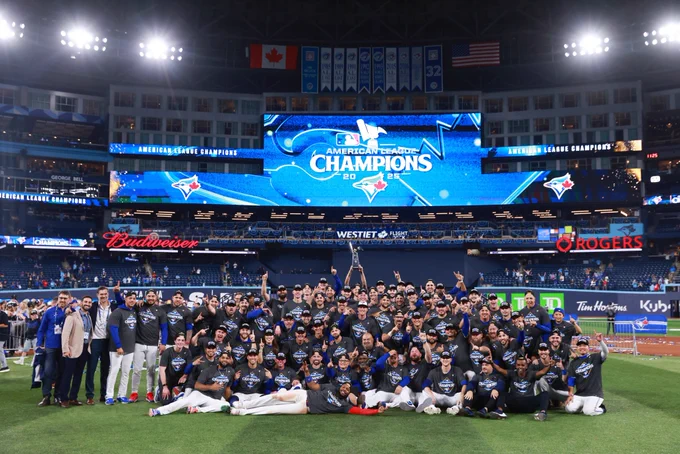 The Toronto Blue Jays pose for a team photo on the field after winning the ALCS. They wears black Blue Jays AL Champs shirts.
