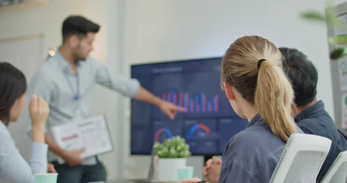 vier Menschen sprechen über Diagramme auf einem großen Monitor. Foto: Kasipat Phonlamai / Moment / Getty Images