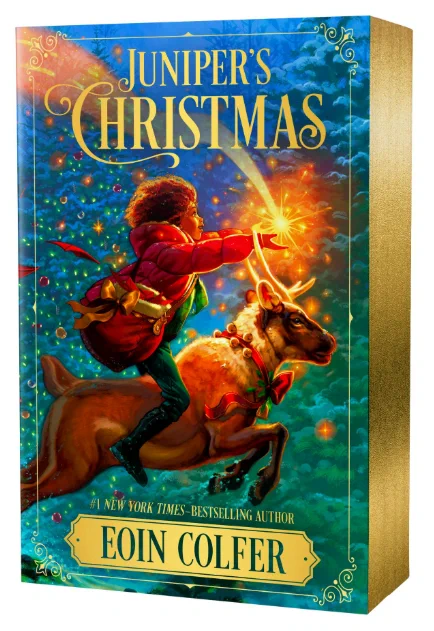 Book cover of "Juniper's Christmas" by Eoin Colfer. A girl rides a reindeer and holds out her hands to catch a golden star. Behind her are pine trees decorated with lights. The book has shiny gold edges. 