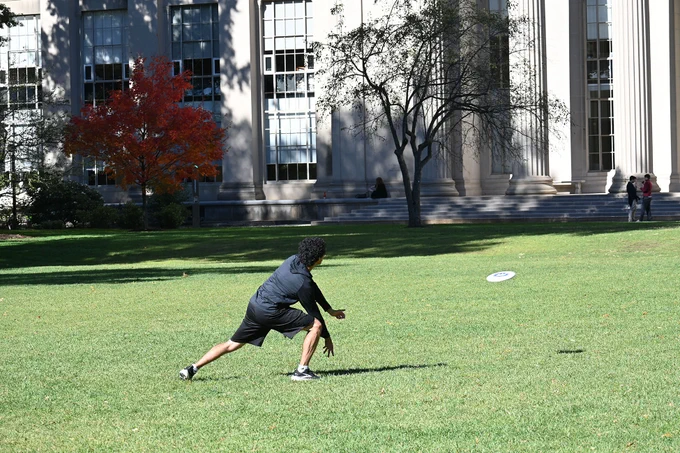 An MIT student throwing a frisbee in front of the great Dome.