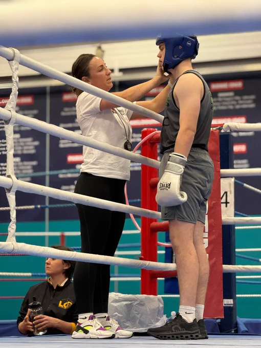 Harriet adjusting the headgear of a boxer in the ring, with another person observing from the corner.
