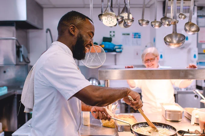 Two chefs, one stirring a pot and another observing, working together in a commercial kitchen.