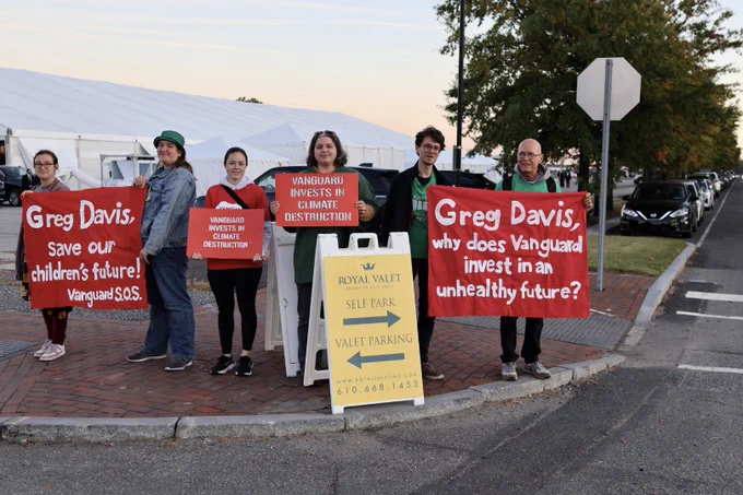 Six people stand outside in front of a valet parking sign, holding red banners and signs about Vanguard's investments. Photo by Laran Kaplan