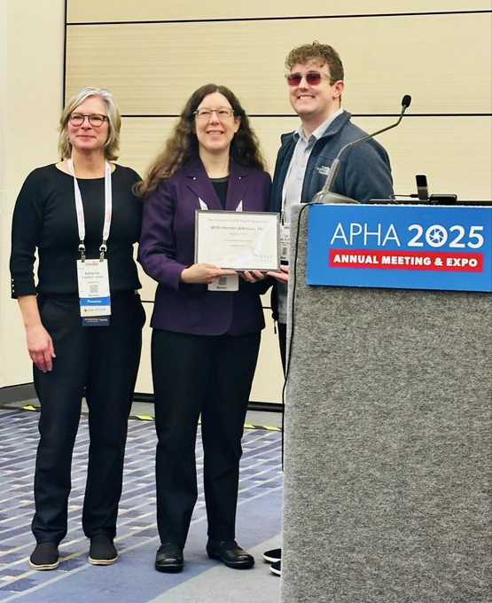Three people stand and smile with award