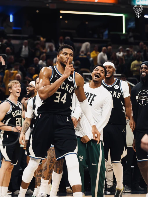 A photo of Giannis putting his finger against his mouth to silence the crowd with his teammates smiling in the background.