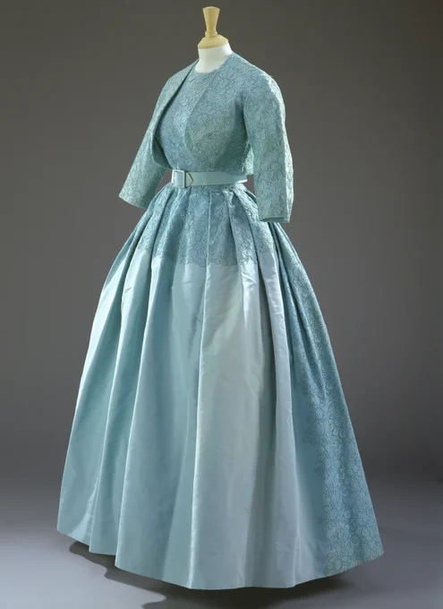 A vintage evening dress displayed on a mannequin, featuring a fitted bodice with a lace overlay and a voluminous skirt in light blue.
