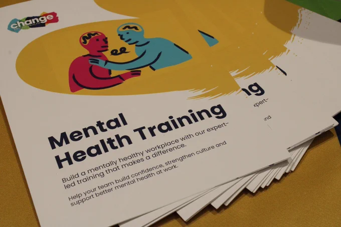 A leaflet that has two animated characters in pink and blue. The leaflet says Mental Health Training: build a mentally healthy workplace with our expert-led training that makes a difference. Help your team build confidence, strengthen culture and support better mental health at work.