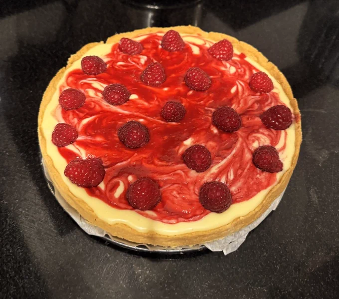 A close up of a white chocolate and raspberry tart, against a black granite benchtop.