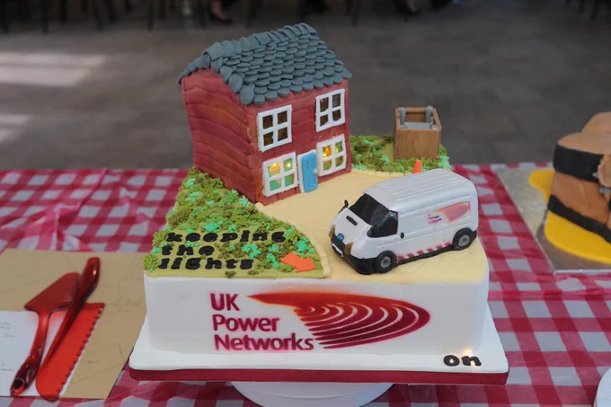 A fondant cake, decorated with a house, driveway and garden. There is also a UKPN van and fondant saying "keeping the lights on".