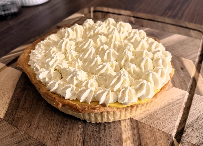 A tropical tart, decorated with cream. It sits on a wooden breadboard.