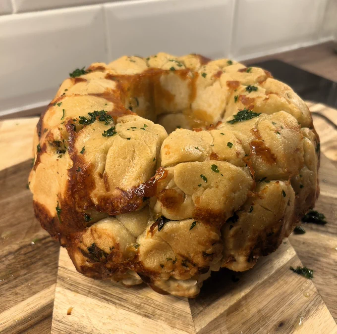 Savoury pull-apart bread. It is garnished with green herbs, and sits on a wooden breadboard.