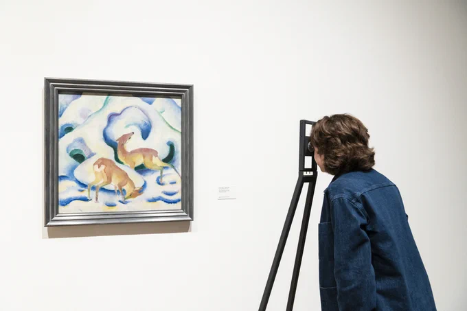 A person looking at a painting of a blue and green snowy landscape with two orange deers.