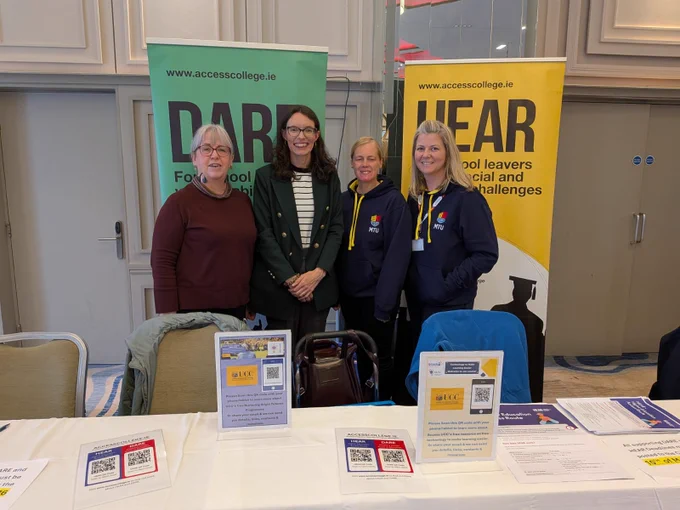 A group of four professionals standing together in front of two exhibition stands at the Career Options Cork event. They are staff from UCC and MTU, and are representing their Access offices at this event.