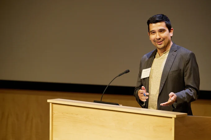 Jason Buenrostro stands behind a podium speaking to an audience.