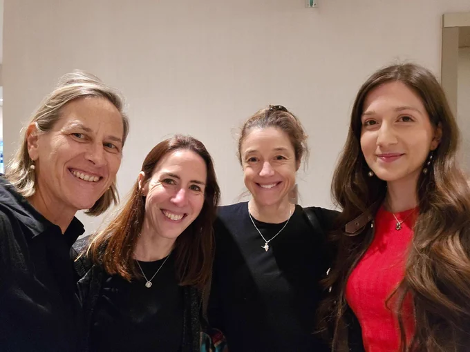 Four individuals smiling for a group photo in an indoor setting with a light background.
