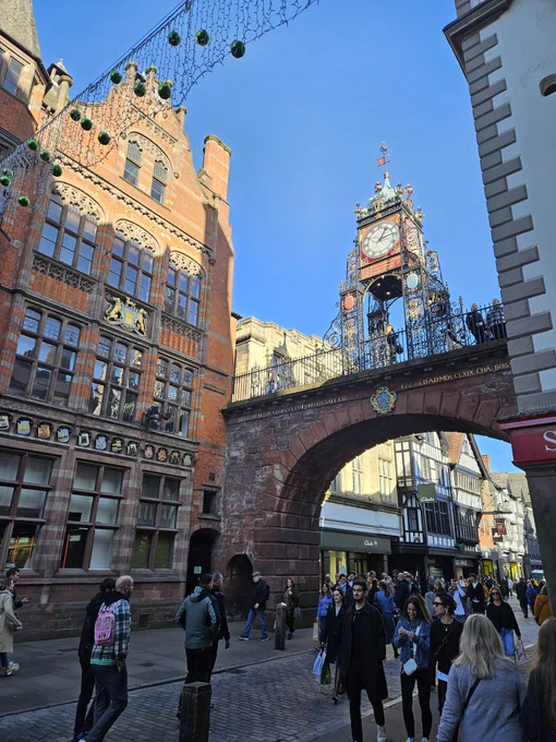 Eastgate, Chester on a sunny day. View of HSBC Bank, Eastgate clock, people on the Chester walls and people walking through the sandstone Eastgate. Blue sky 