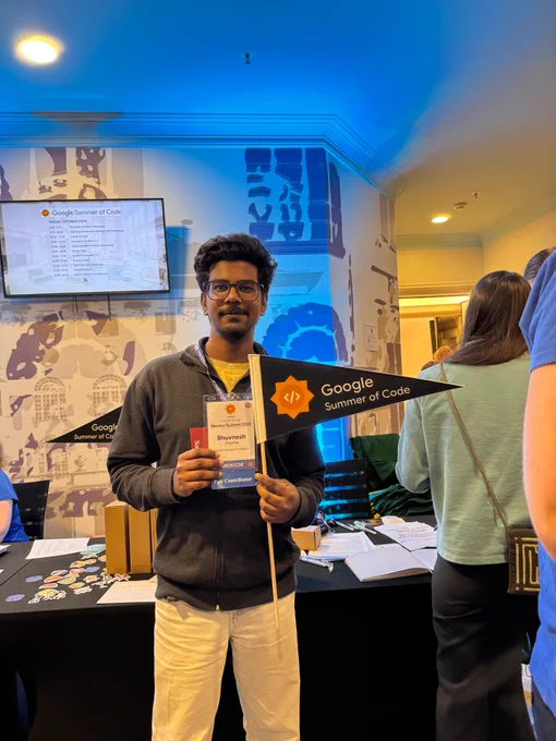 Bhuvnesh standing in front of the registration stand, holding his mentor summit badge and a Google Summer of Code flag