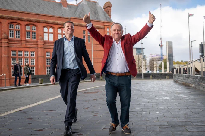 Lindsay Whittle with arms raised gives two thumbs up walking with Rhun ap Iorwerth towards the Senedd