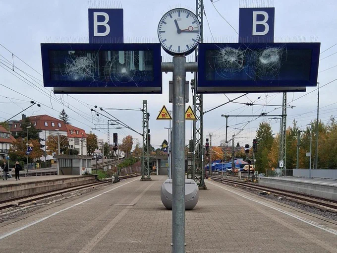 Das Bild zeigt den Bahnsteig des Bahnhofs Stuttgart-Vaihingen mit zwei stark beschädigten Anzeigetafeln, einer Uhr dazwischen und Gleisen im Hintergrund.