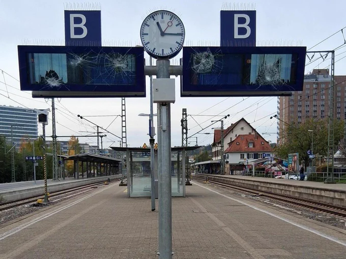 Das Bild zeigt den Bahnsteig des Bahnhofs Stuttgart-Vaihingen mit zwei stark beschädigten Anzeigetafeln, einer Uhr dazwischen und Gleisen im Hintergrund.