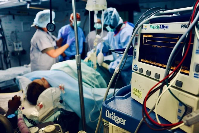 A team of medical professionals in surgical scrubs working under bright lights in an operating room representing trauma and emergency care research.