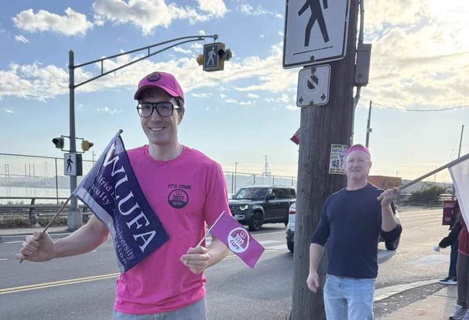 A photo of Cameron McKenzie holding a WLUFA and CUPE 3912 flag with Michael Arfken from UPEIFA in the background