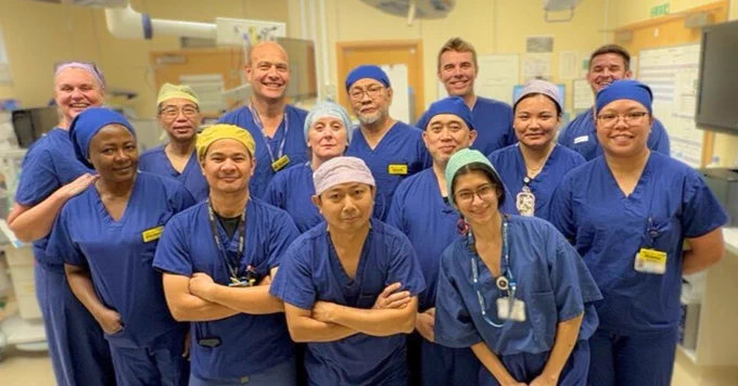 Group of healthcare professionals in scrubs and surgical caps, smiling in a hospital setting.