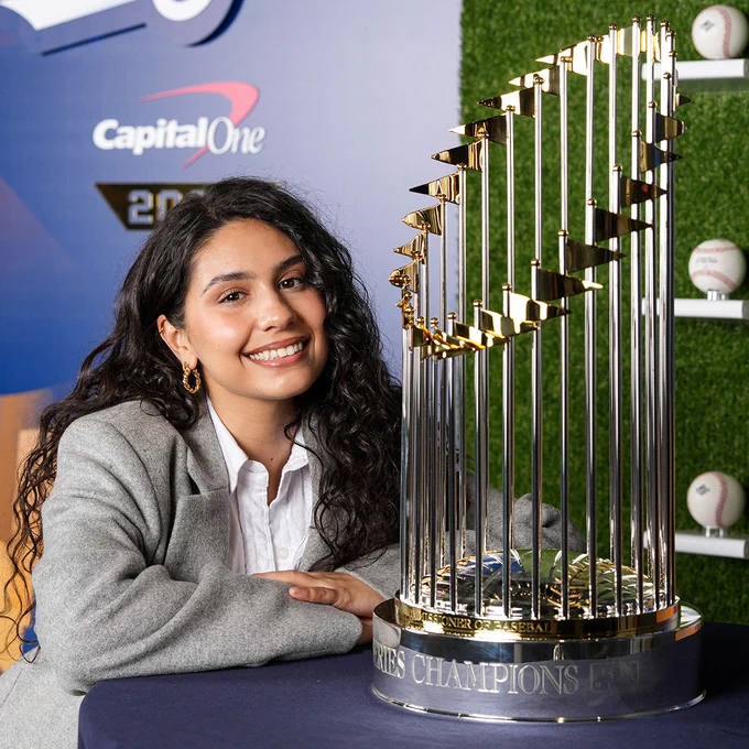 Alessia Cara posing for a photo next to the World Series trophy. She's wearing a gray jacket and a white shirt.