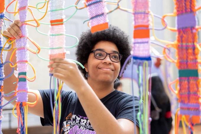 Person holding up colourful knitted strips as part of a science public engagement project