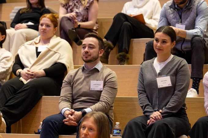 Audience members sit in bleacher-style seating listening to a speaker off camera