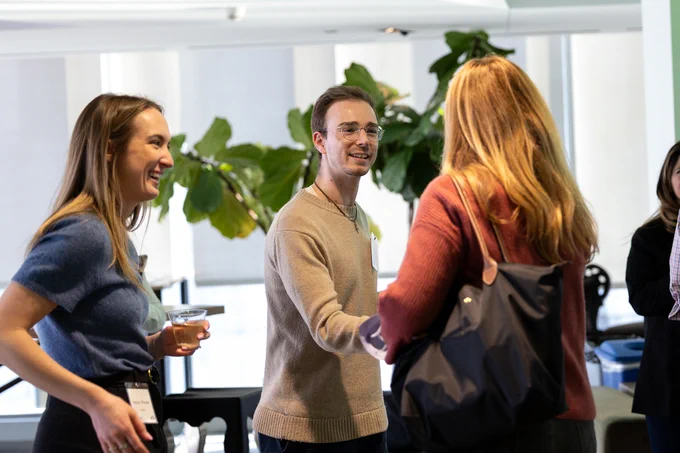A young man smiles while shaking hands with a young woman