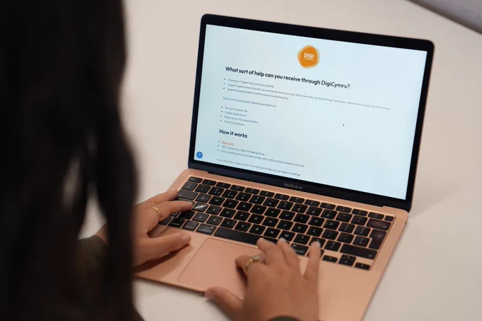 A woman out of focus looking at her laptop. She’s looking at the DigiCymru page on the ProMo Cymru website