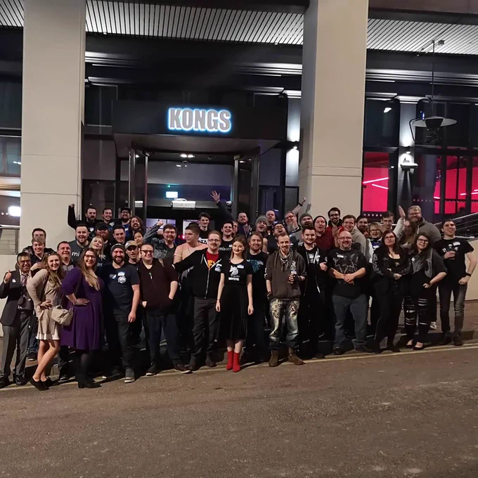 Photo of a big bunch of around 50 people cheering & stood infront of a building with the logo "Kongs" on a main street/road.