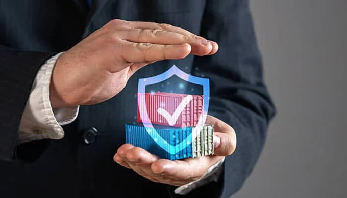 A businessman’s hands form a protective gesture around stacked cargo containers with a digital shield and checkmark icon, symbolizing cargo protection, supply chain security, and logistics safety.