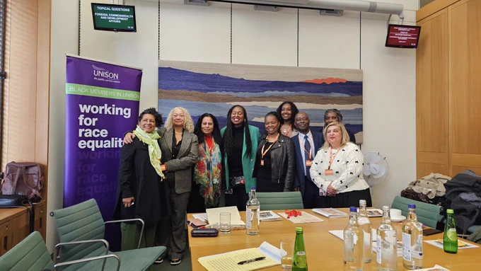 A group of activists in a parliamentary room in front of a banner of Unison Working for Race Equalities